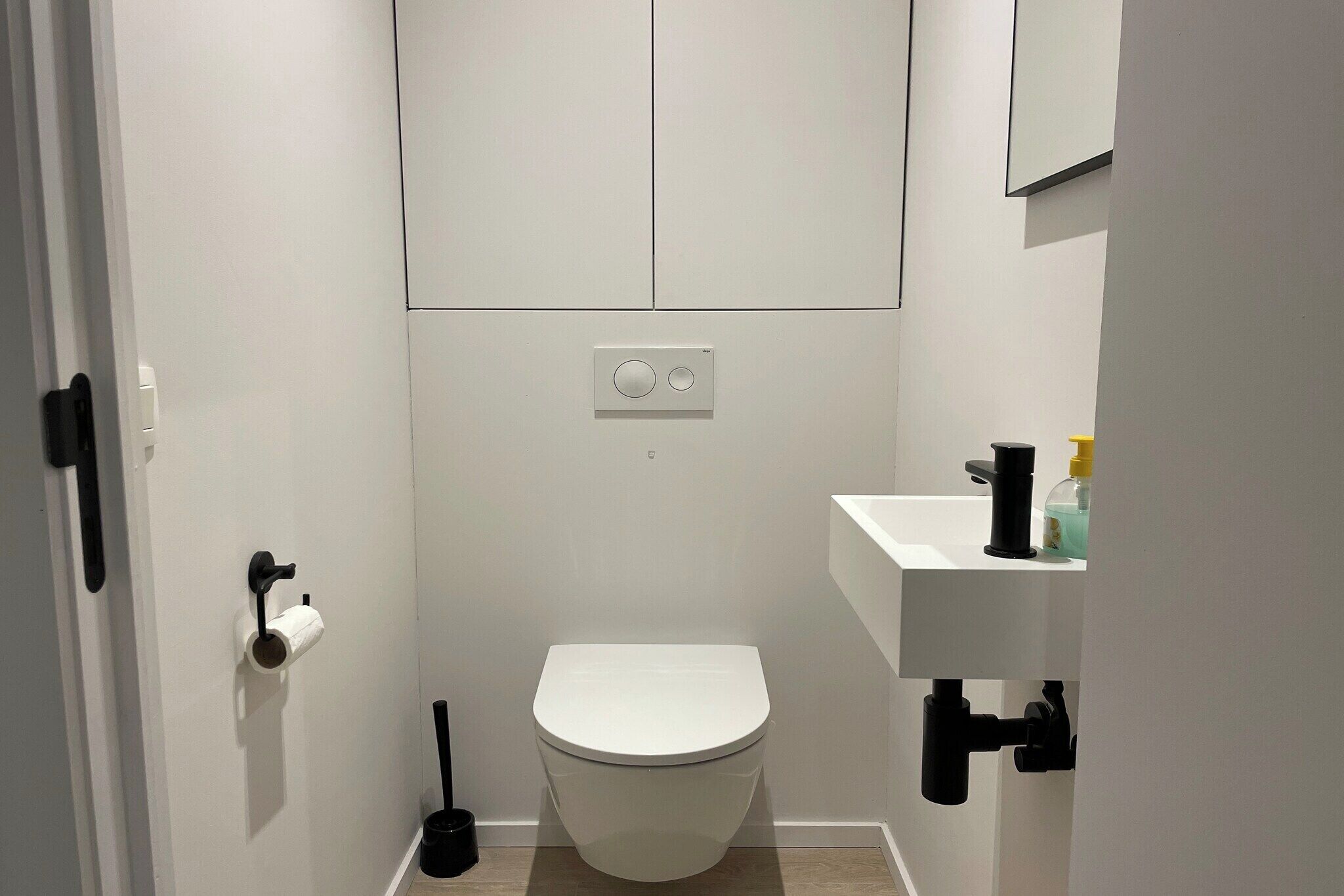 Een kleine, moderne badkamer met toilet, handdroger, wastafel en spiegel.