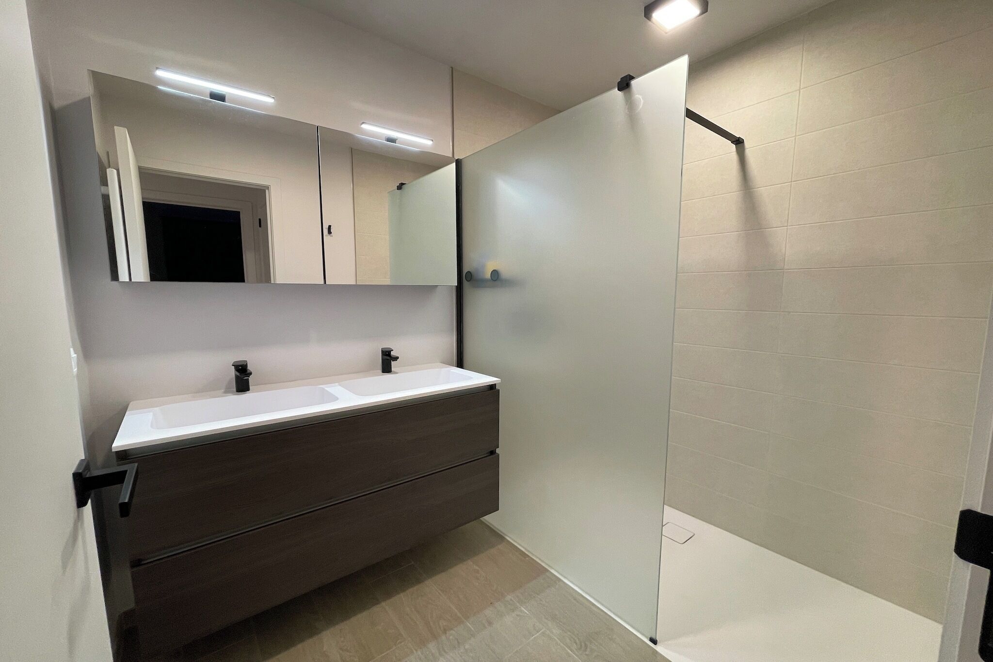 A modern bathroom with a large mirror, a double sink vanity, and a glass shower enclosure.