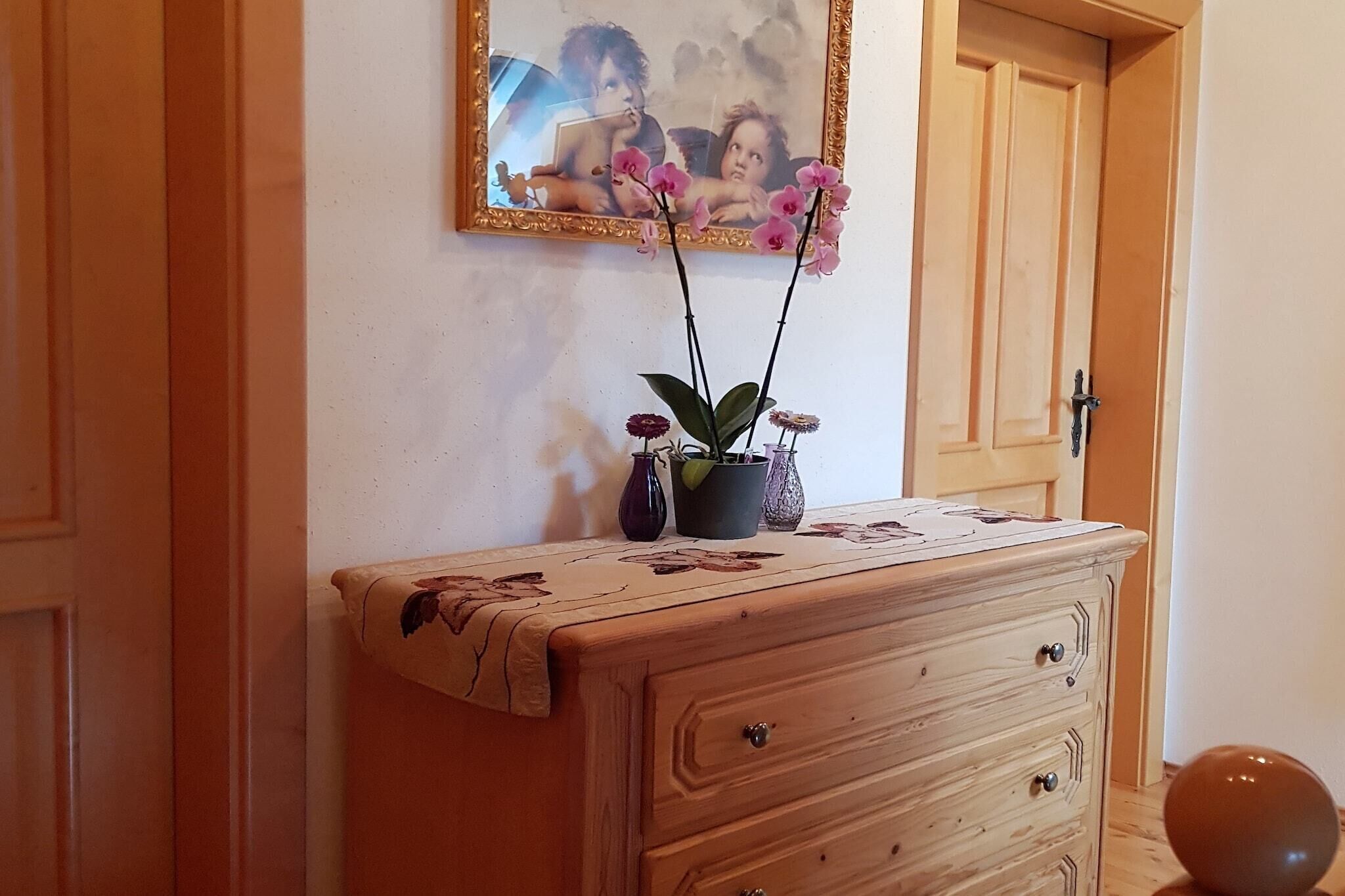 En byrå i trä med lådor, ett bordsöverdrag med blommönster och två orkidéer i krukor.