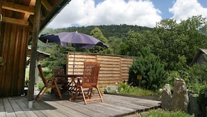 A wooden deck with a table and chairs, an umbrella, and a view of a forested hill. - Chalet in Einach near Ski Slopes (Stadl an der Mur)