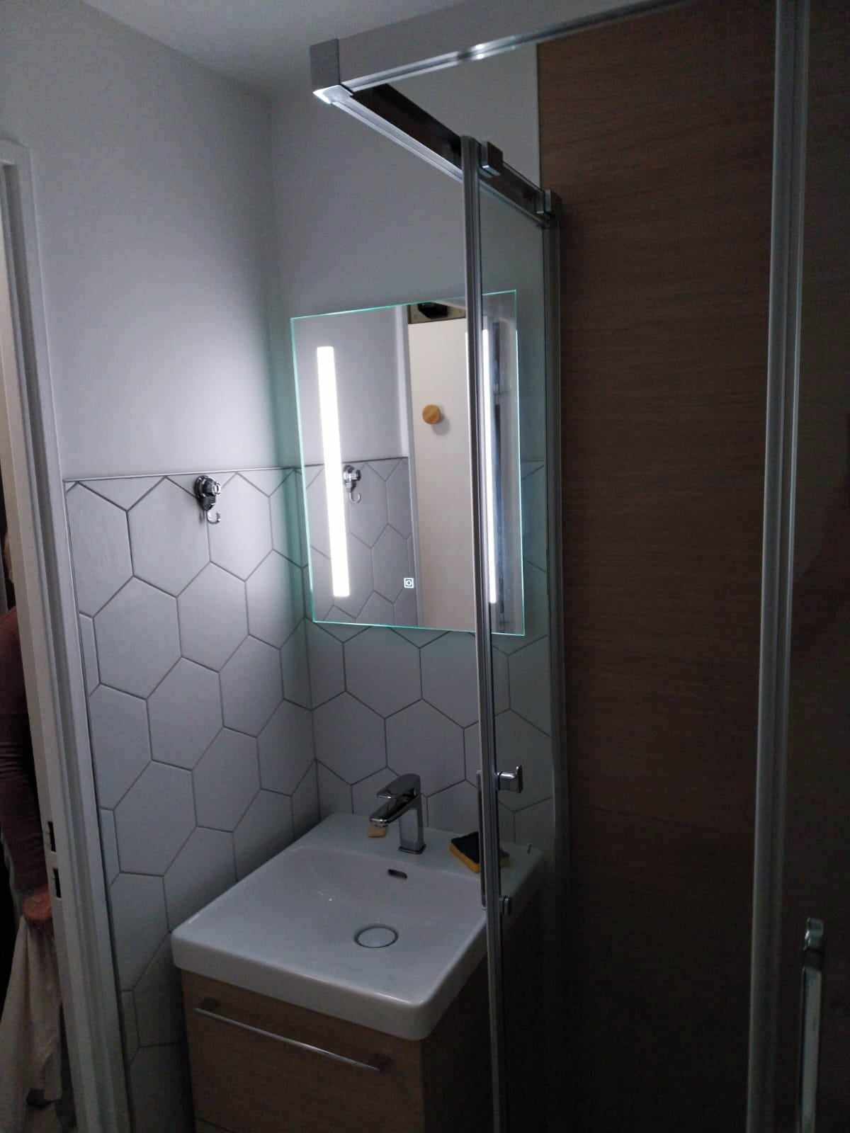 A bathroom with a glass shower enclosure, a white sink with a mirror, and hexagonal tile walls.