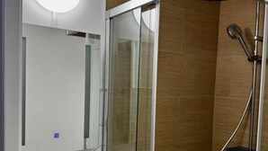 A modern bathroom with a glass shower enclosure, a white sink with a mirror, and a round light fixture above the mirror.