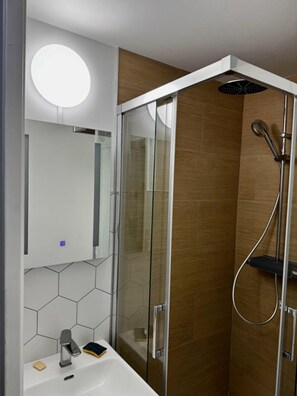 Un baño moderno con cabina de ducha de vidrio, un lavabo blanco con espejo y una lámpara redonda sobre el espejo.