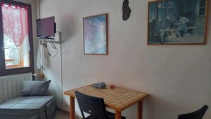 A small room with a bed, a table with chairs, a TV, and two framed pictures on the wall.
