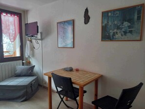 Una habitación pequeña con una cama, una mesa con sillas, un televisor y dos cuadros en la pared.