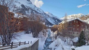 A snow-covered mountain landscape with a river flowing through a concrete channel, surrounded by wooden buildings and bare trees.