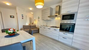 Een moderne keuken met inbouwapparatuur, een eethoek met een tafel en stoelen, en een bank op de achtergrond.