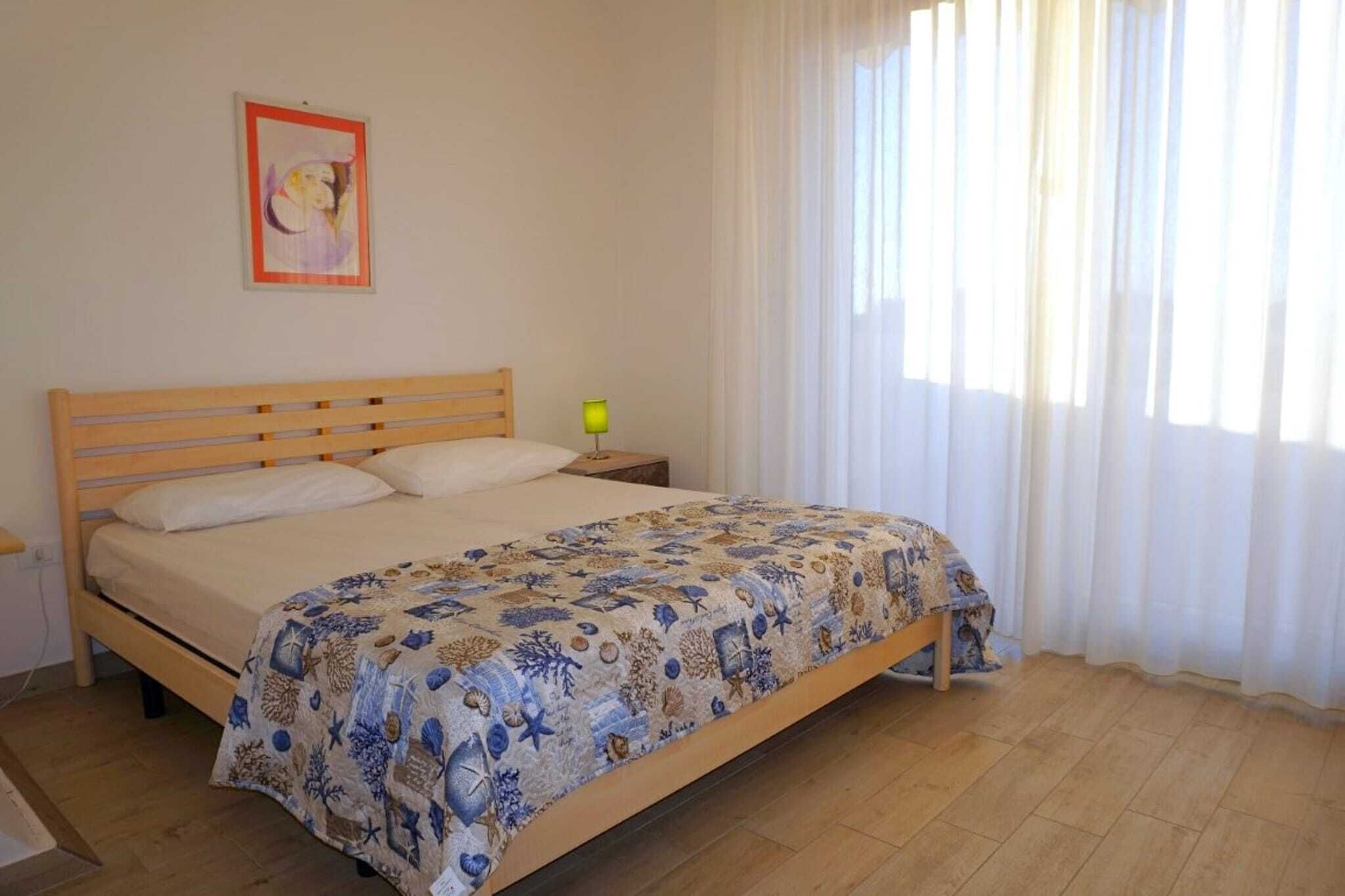 A bedroom with a wooden bed, a nightstand, a lamp, and a window with sheer curtains.