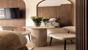 A modern room with a round table, two chairs, a TV mounted on a wooden panel, and a large mirror reflecting a wardrobe. - Charming Studio - 2P- Madeleine (Paris)