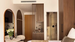 A modern hotel room with a bed, a round table with a vase of flowers, a mirror, and a shower area. - Charming Studio - 2P- Madeleine (Paris)
