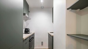 Una cocina estrecha con una cafetera en la encimera, un extractor en el techo y un ventanal pequeño.