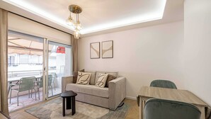 Una sala moderna con sofá, mesa de comedor y una silla. Hay un ventanal corredero que da a un área exterior con sillas.