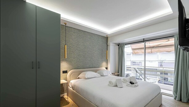 Una habitación de hotel moderna con una cama grande, un armario, un televisor de pantalla plana y un balcón con vistas.