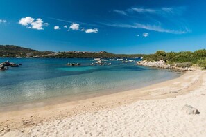 A beach with clear turquoise water, sandy shore, and rocky outcrops.