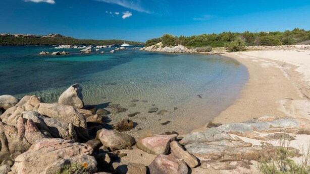 A coastal beach with clear turquoise water, rocky shoreline, and distant hills. - Apartment in Marinella near the beach (Marinella)