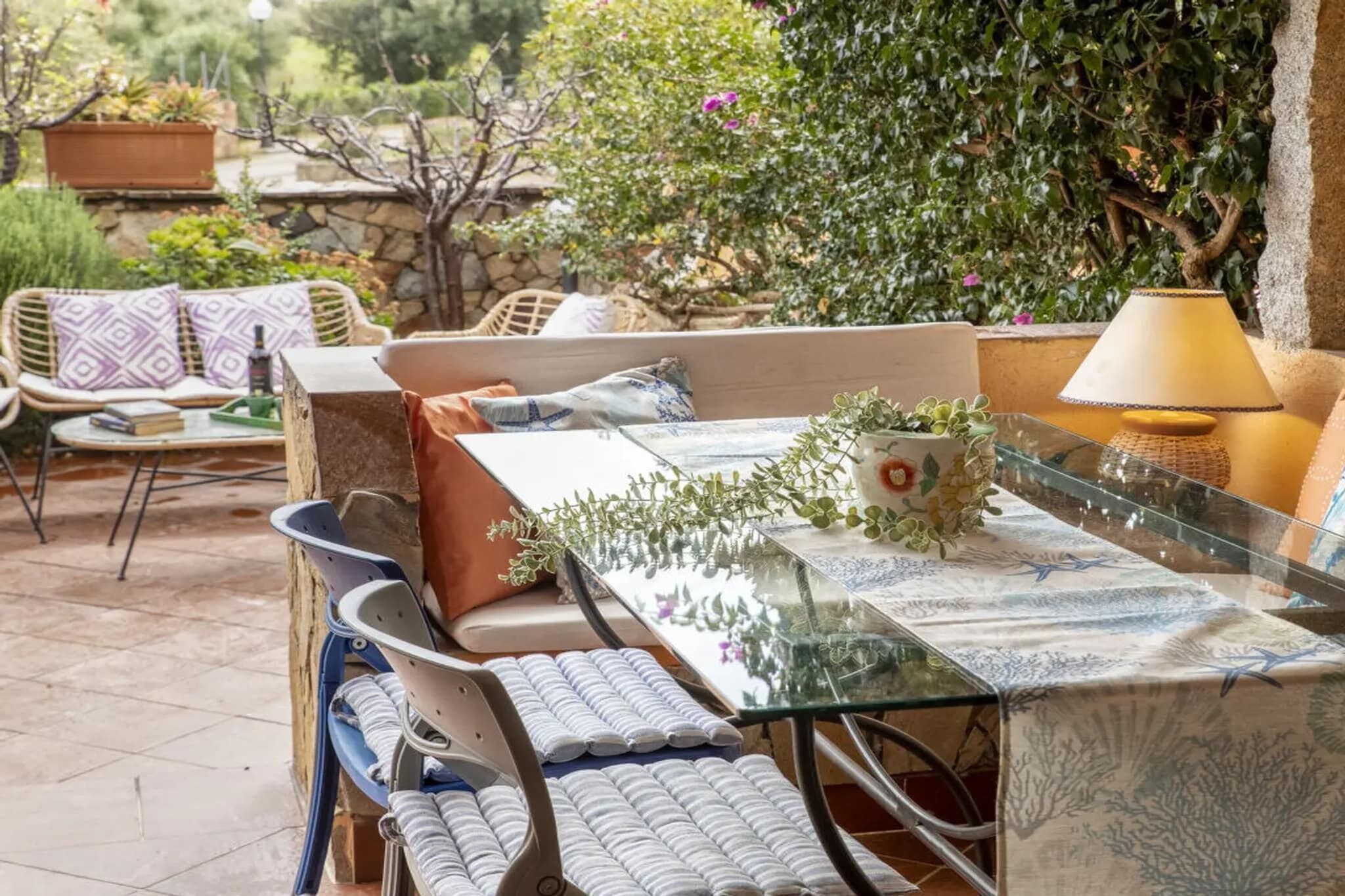 A patio with outdoor furniture, a glass table, and potted plants.