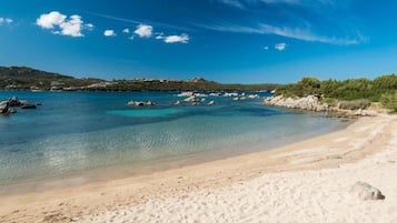 Una spiaggia con acque cristalline turchesi, una costa sabbiosa e affioramenti rocciosi.