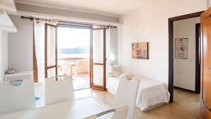 A room with a bed, a table, and chairs, a balcony with a view, and a door leading to another room. - Apartment in Sardinia near stunning beaches (Marinella)