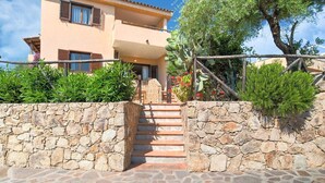A two-story building with a stone wall and a staircase leading to the entrance. - Apartment in Sardinia near stunning beaches (Marinella)
