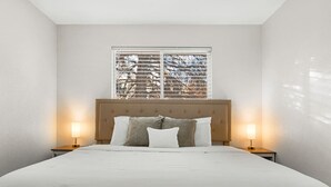 A neatly made bed with a wooden headboard, two bedside lamps, and a window with blinds. - Modern Family Friendly Escape|Central|5-Bedroom (Denver)