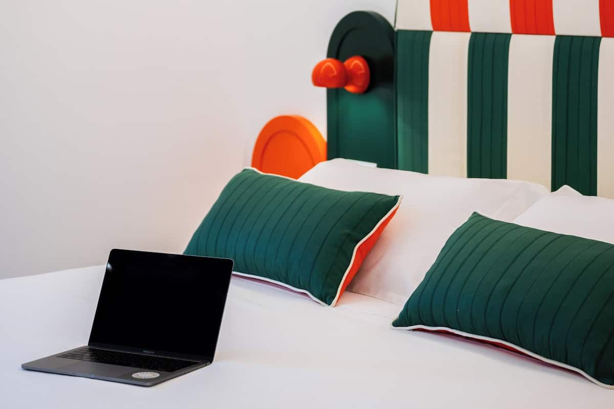Een bed met een laptop, groene kussens en een gestreept hoofdeinde.