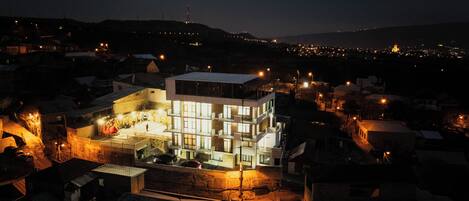 A modern multi-story building with a flat roof, surrounded by smaller houses.