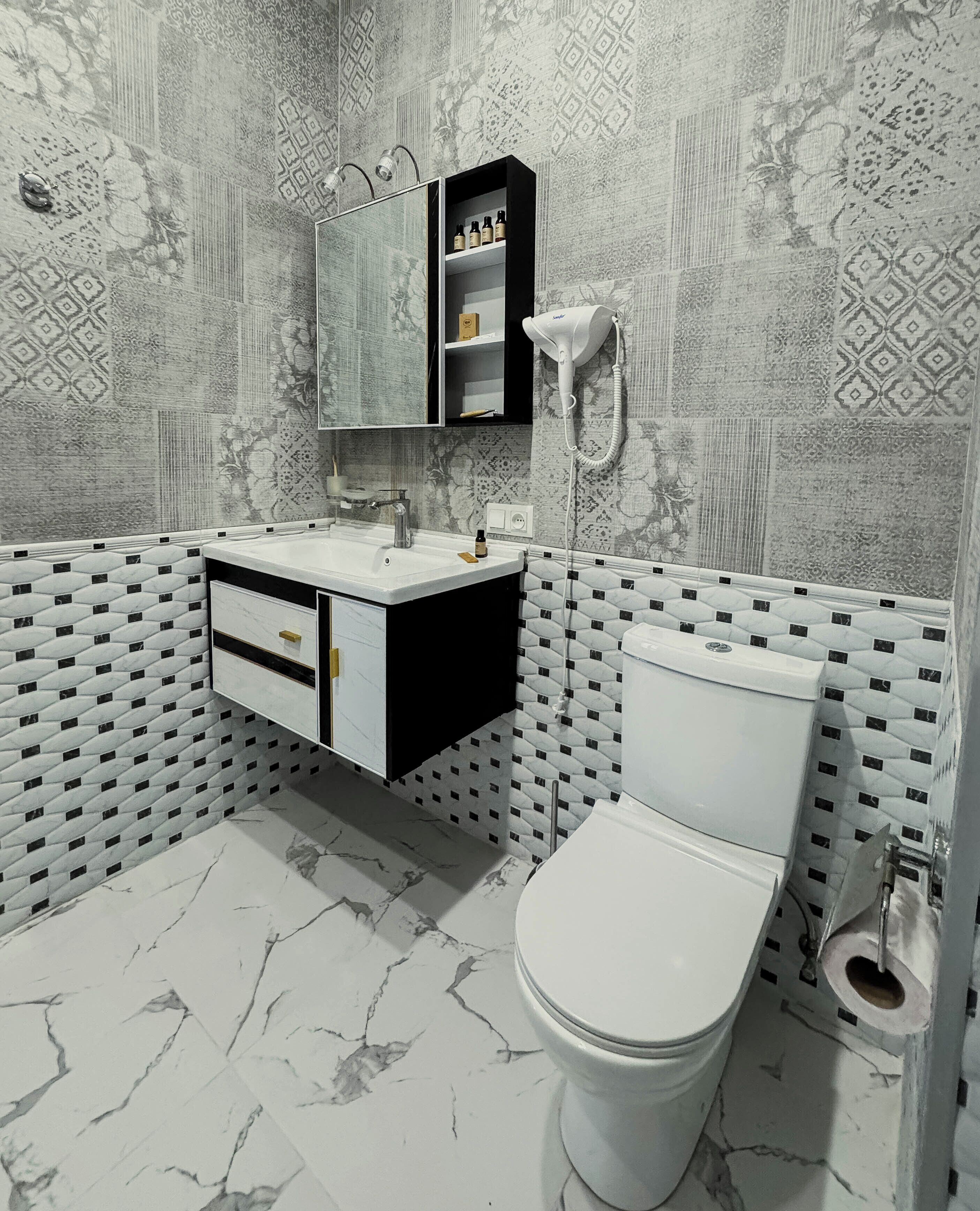 Een badkamer met een wit toilet, een zwart-wit wastafelmeubel en een behangen muur.