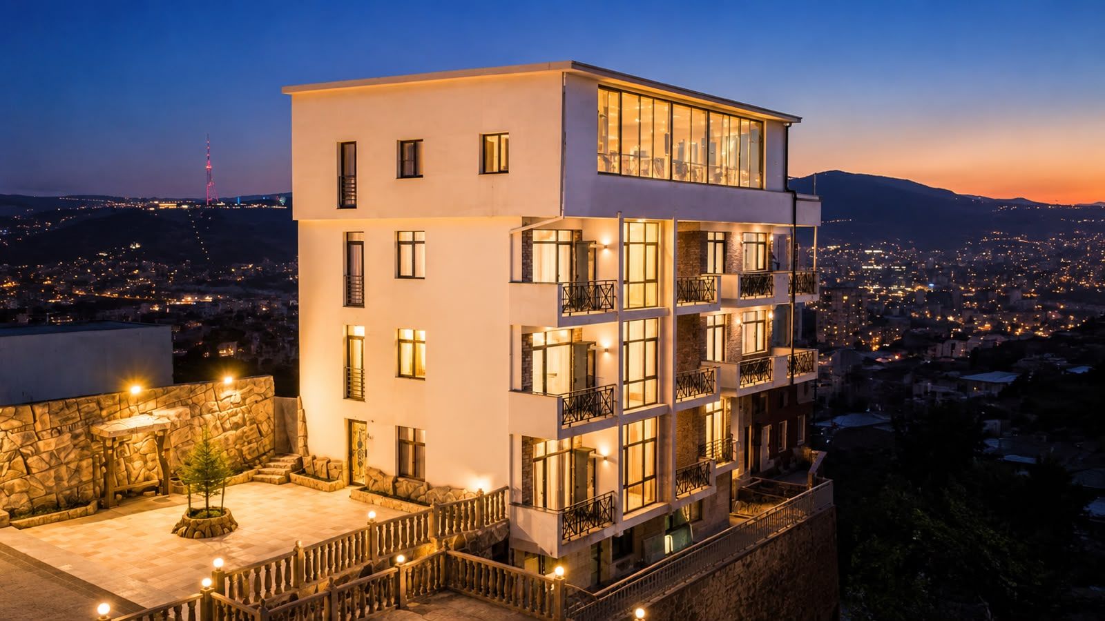 A multi-story hotel with balconies and a view of a cityscape at dusk.