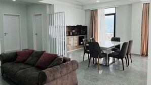 Una sala de estar moderna con un sofá, una mesa de comedor con sillas, una zona de cocina y un amplio ventanal con cortinas.