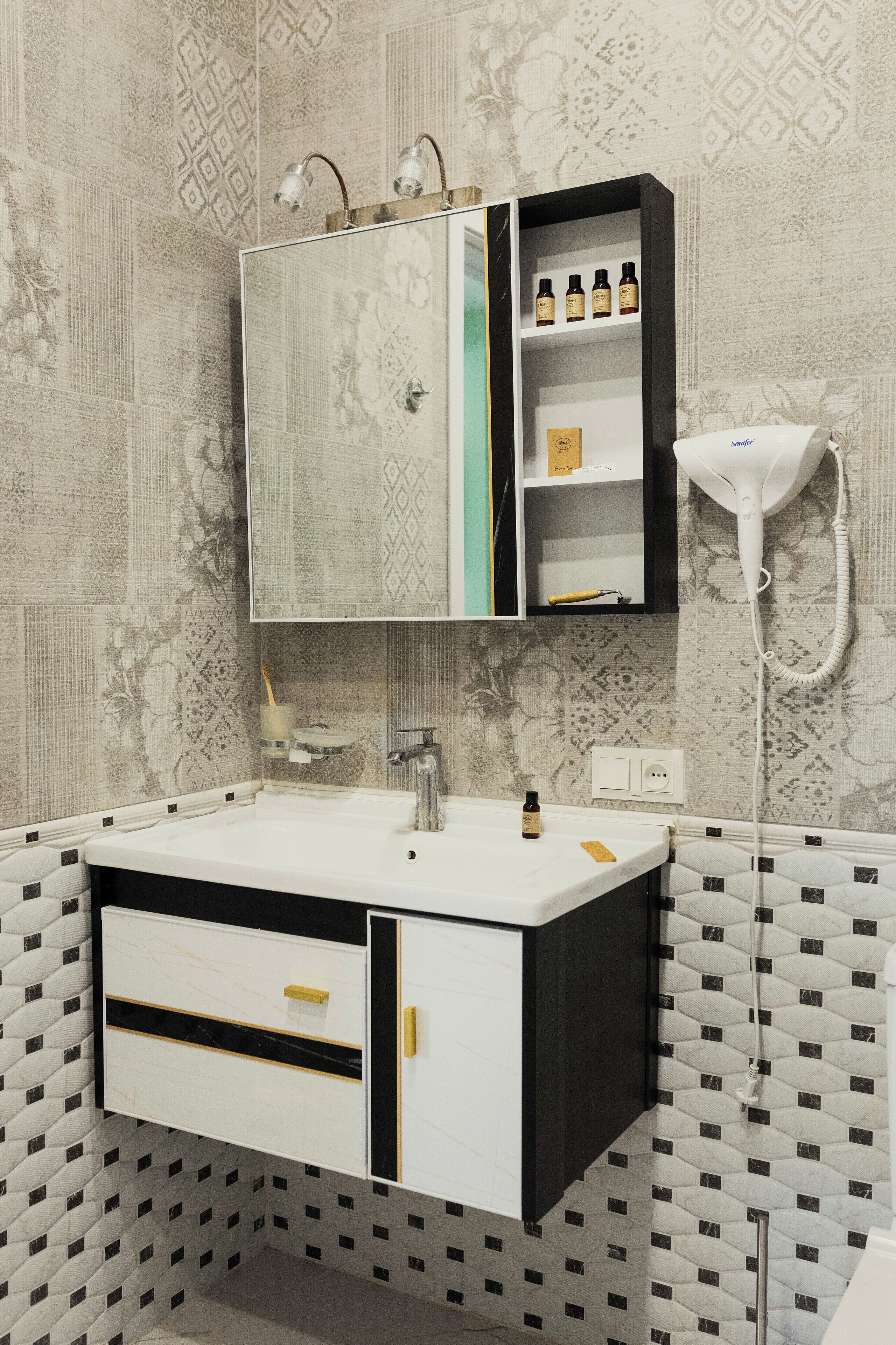 A bathroom with a white sink, black and white cabinet, and patterned wallpaper.