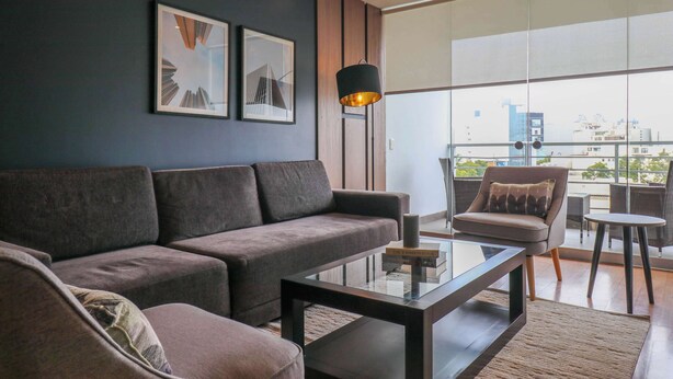 A modern living room with a sofa, coffee table, and a chair. There are two framed pictures on the wall and a floor lamp. - w* | Classy 2BR in Miraflores (Miraflores)