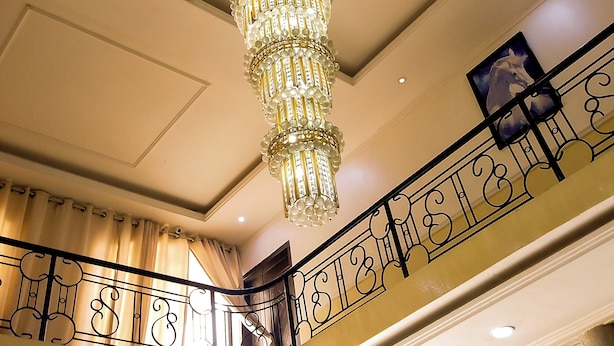 A chandelier with multiple tiers of lights, a balcony with ornate railing, and a sign for breakfast menu. - Dreamland suites (Abuja)