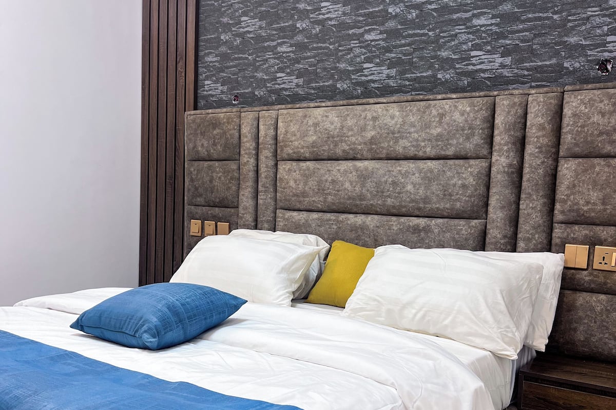 A neatly made bed with white and blue bedding, a wooden headboard, and a textured wall behind it.