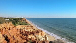 Un paisaje costero con playa, acantilados y un horizonte urbano distante.