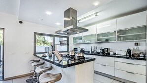 Una cocina moderna con una isla central, taburetes de bar y un ventanal grande.