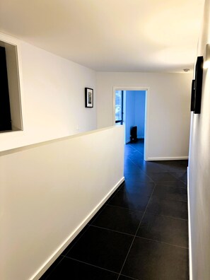 A hallway with white walls and black tiled flooring, leading to a room with a blue door. - 150m Walk to Beach, WiFi & Fireplace | Salt & Sand (Lilli Pilli)