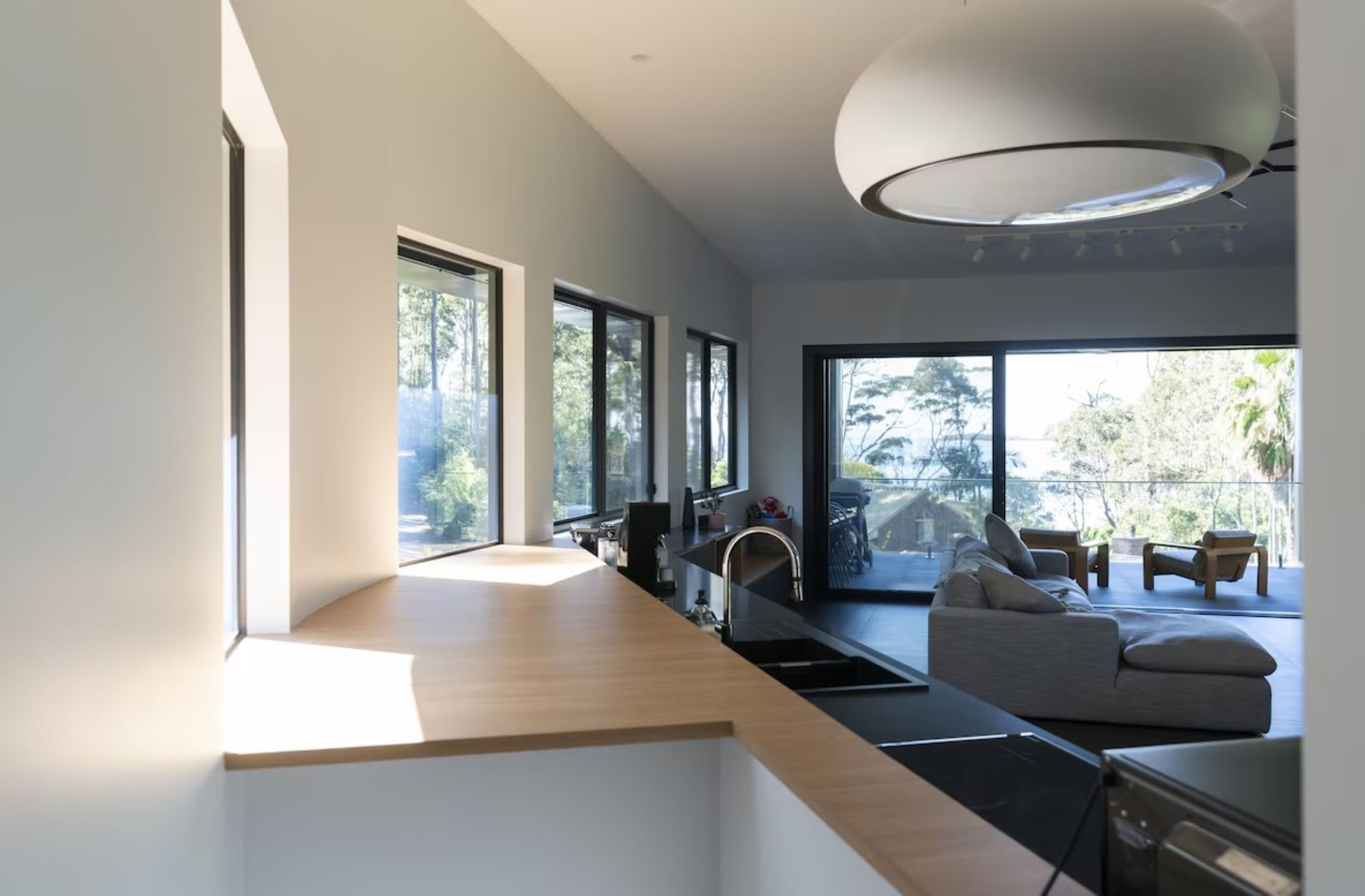 A modern kitchen with large windows, a dining area with a sofa, and a view of the outdoors.