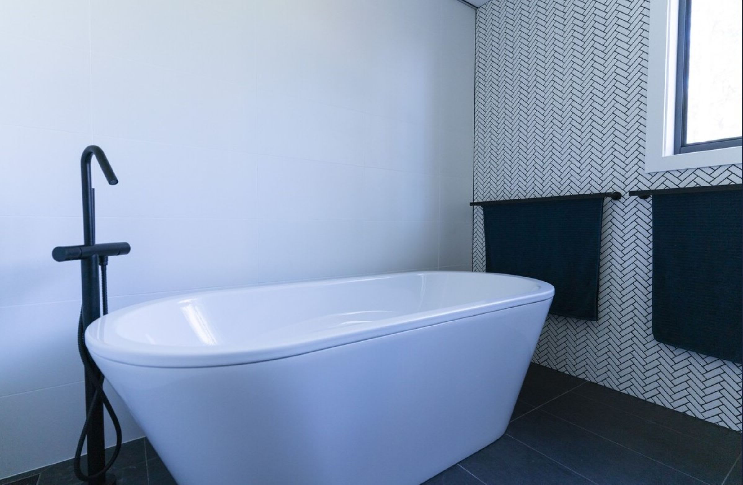 Ein modernes Badezimmer mit einer freistehenden Badewanne, einem schwarzen Wasserhahn und einem Fenster mit Aussicht.