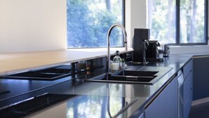 Une cuisine moderne dotée d’un évier en acier inoxydable, d’une machine à café et d’une fenêtre offrant une vue sur la verdure environnante.