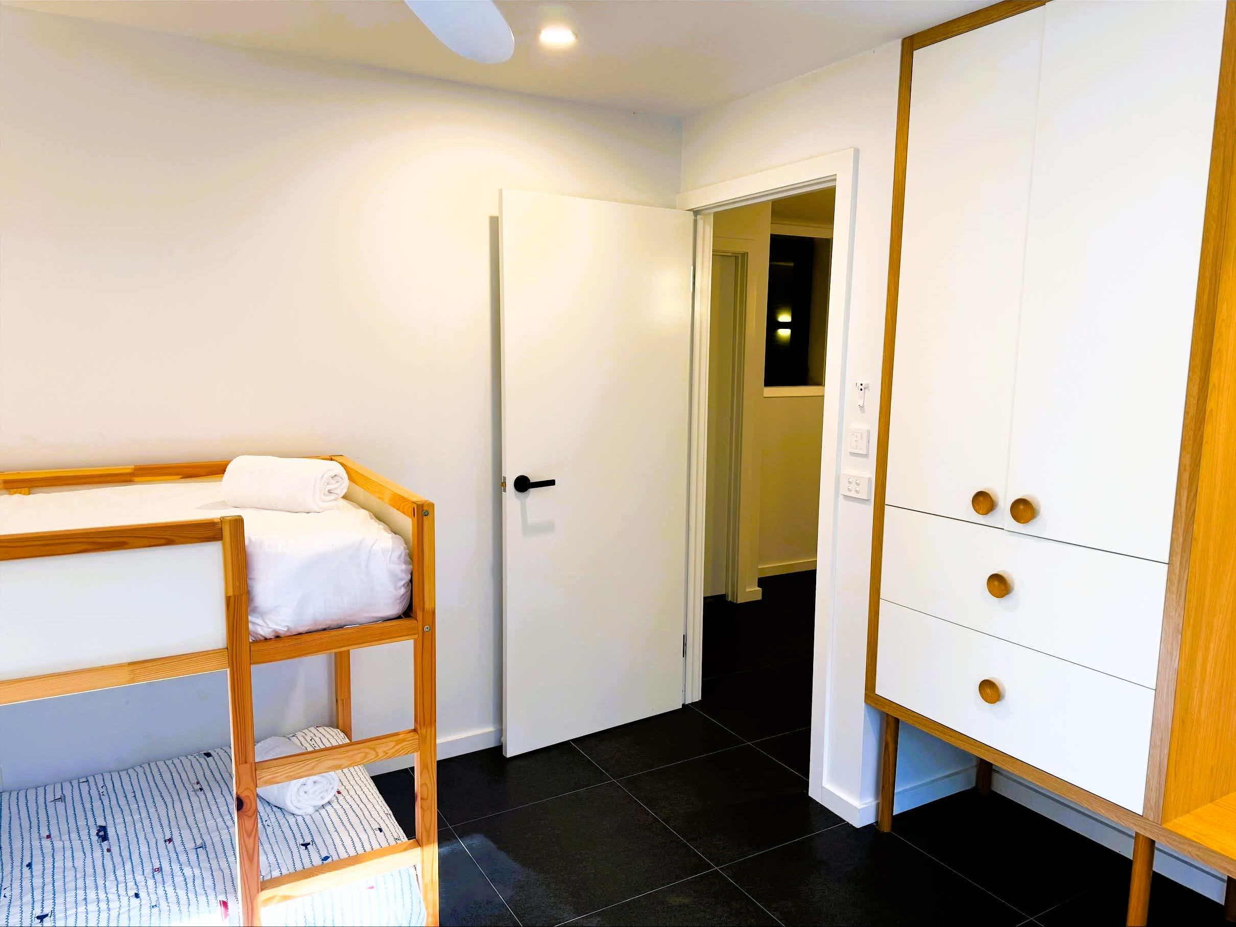 Una habitació amb un llit superposat, un armari i una porta que dona a una altra habitació.