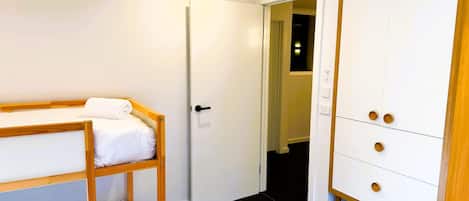 A room with a bunk bed, a wardrobe, and a door leading to another room.
