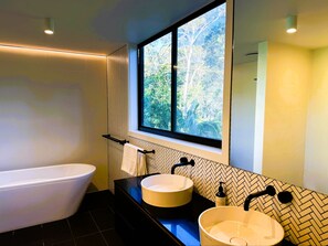 A modern bathroom with a freestanding bathtub, a large mirror, and a window with a view of trees.