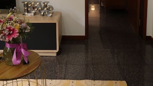 Une pièce avec un plancher en bois, une télévision sur la gauche, un meuble orné des lettres « LOVE », un vase avec des fleurs et un miroir sur la droite.