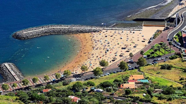 Vue aérienne d’une plage avec une digue rocheuse, un rivage sablonneux et une route menant à un parking.
