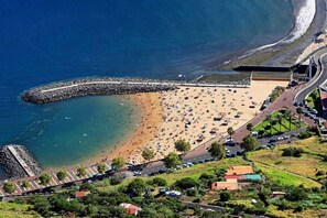 Vista aèria d'una platja amb un espigó rocos, una riba sorrenca i una carretera que condueix a una zona de pàrquing.