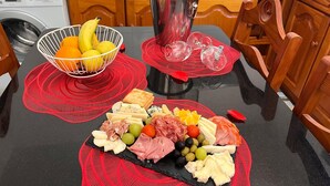 Un plan de travail de cuisine avec un panier de fruits, une bouteille de vin et une planche de charcuterie.