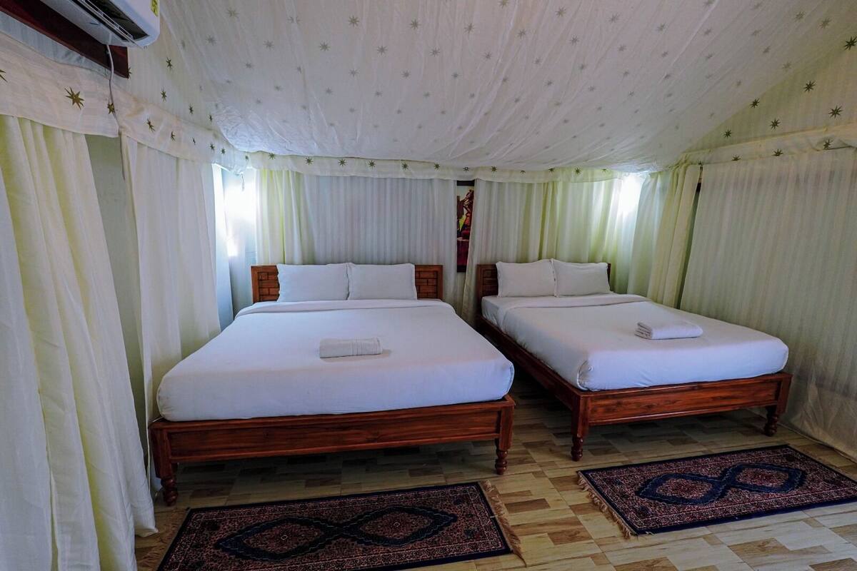 A room with two wooden beds, white bedding, and patterned rugs.