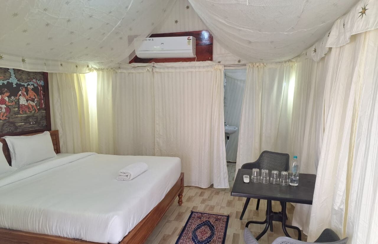 Ein Hotelzimmer mit Bett, Tisch mit Gläsern und einer Flasche sowie einem Deckenventilator.