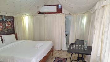 Ein Hotelzimmer mit Bett, Tisch mit Gläsern und einer Flasche sowie einem Deckenventilator.