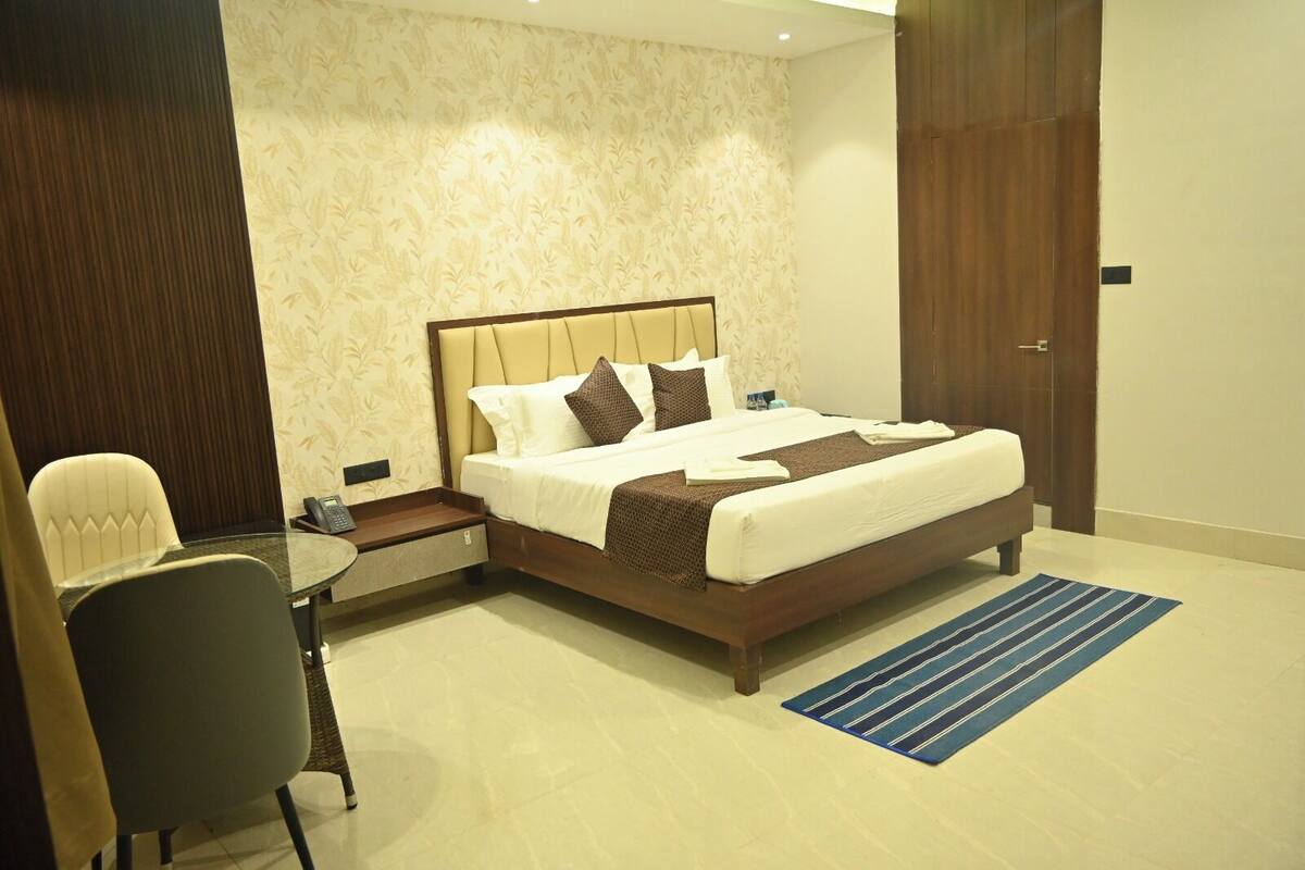 A hotel room with a bed, bedside table, chair, and a small table with a telephone.